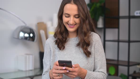 Smiling Young Woman is Using Smartphone in the Office