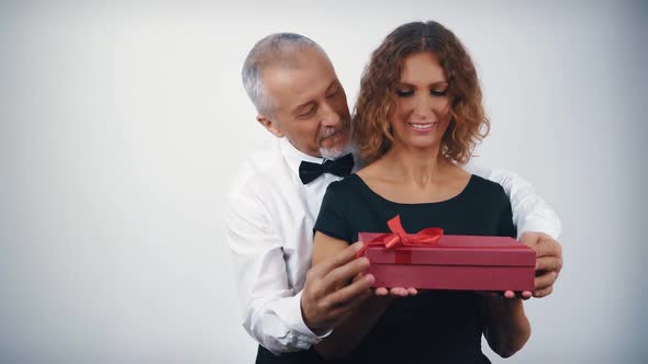 A Middleaged Husband in Love Gives a Gift in a Gift Box to a Beautiful Enthusiastic Wife for
