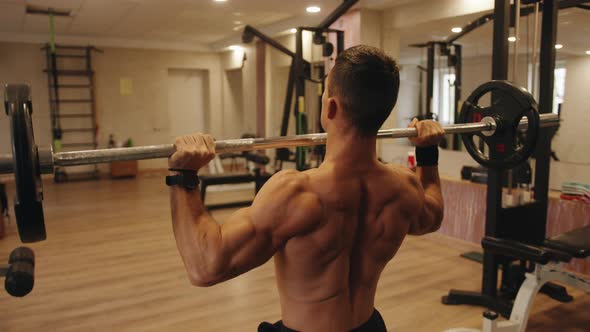 Closeup the Back of a Young Muscular Man in the Gym Doing a Barbell Press From the Chest Sitting on