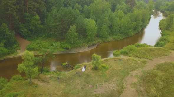 Newlywed Couple on Bank of River at Green Forest Aerial View