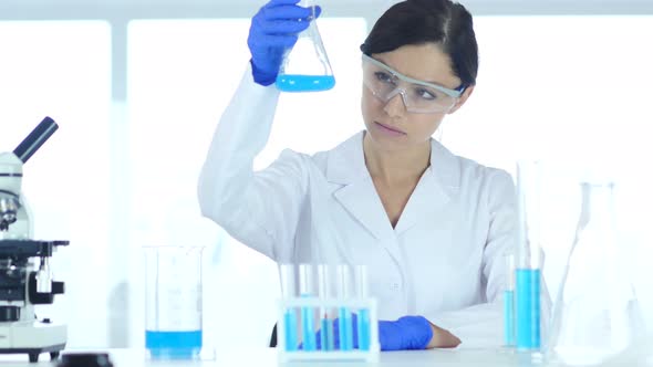 Scientist Holding and Looking at Blue Solution in Flask alt