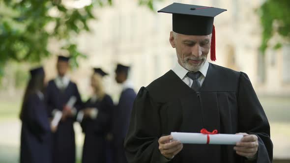 Senior Man in Academic Regalia Holding Diploma, Education at Any Age, New Degree