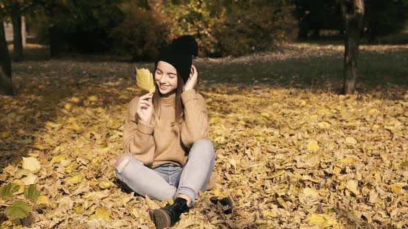 Young Girl Poses with Autumn Leaf at Camera in Park