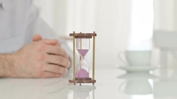 Hourglass on a Table Next To Hands of a Man Waiting Impatiently 