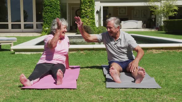 Happy caucasian senior couple exercising practicing yoga in garden in the sun high fiving