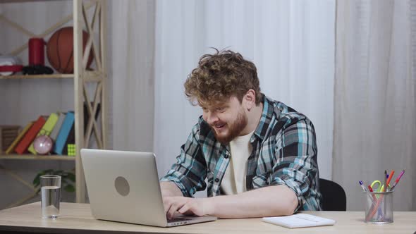 Young Man in Checkered Shirt Typing on Laptop Keyboard and Enjoying