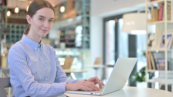 Young Businesswoman with Laptop Pointing at Camera in Cafe