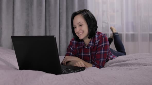 Young Woman Lying on Bed and Having Video Chat Using Webcam on Laptop Computer