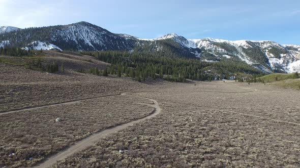 Aerial shot of hiking trail in a meadow below a scenic mountain.