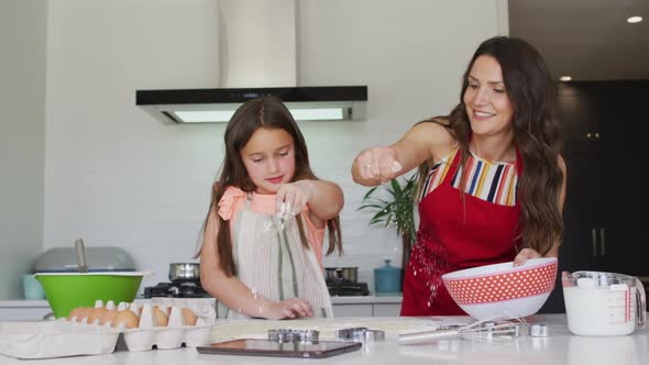 Happy caucasian mother and daughter baking together in kitchen