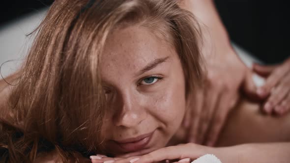 Young Woman with Blue Eyes Receiving a Massage and Looking in the Camera