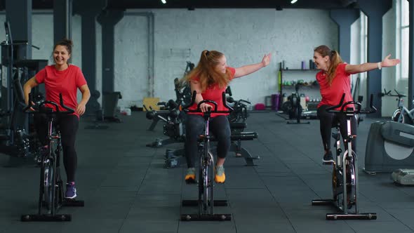 Group of Smiling Friends Women Class Exercising Training Spinning on Stationary Bike at Modern Gym