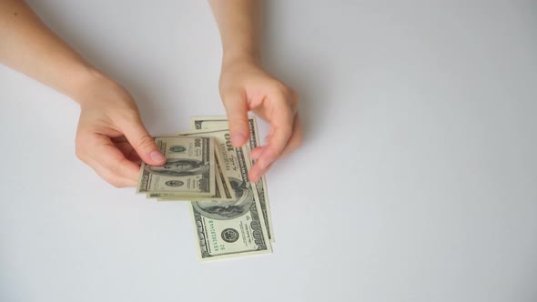 A Woman Counts Dollar Bills for 100 Dollars on a White Background Top View