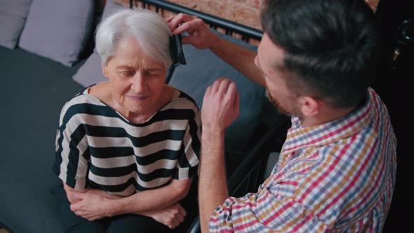 Adult Caucasian Son Taking Care of His Elderly Mother By Combing Her Short Grey Hair