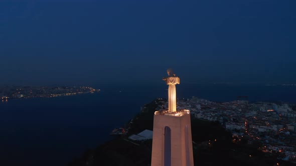 Night Drone Flying Around Big Illuminated Statue of Jesus on Pedestal Above River