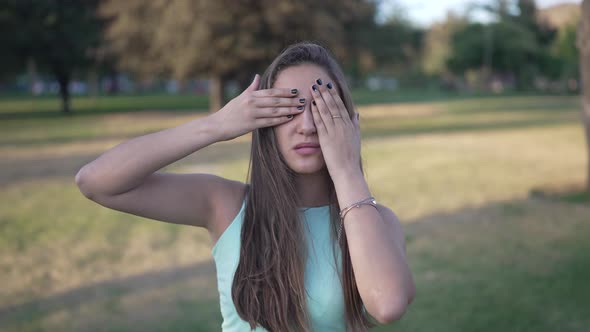 a Cute White Girl Covers Her Eyes with Both Arms in a Park Near the City