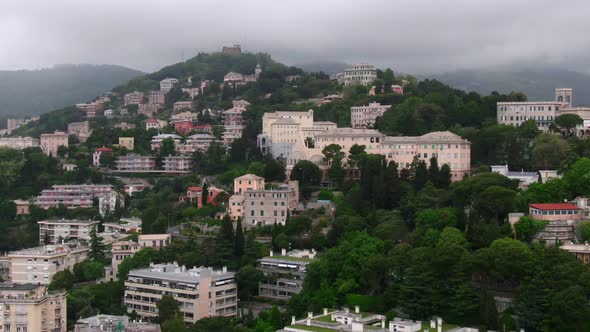 Hillside full of buildings with green vibrant trees on moody stormy day, aerial cinematic view