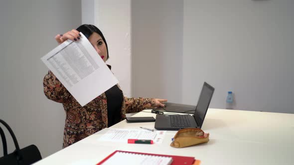 Female worker showing document while working on laptop