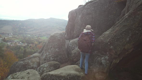Rear View Girl Hiker in Casual Wear with Backpack Walks to Edge of Cliff Enjoys a Beautiful Scenery