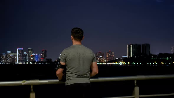 Young Male Sportsman with Athletic Body is Running on the Pier Near the Sailing Ship at Night