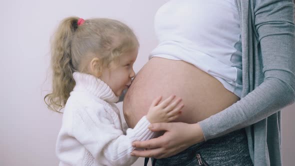 Little Girl Hugs Pregnant Mother on White Background in Room