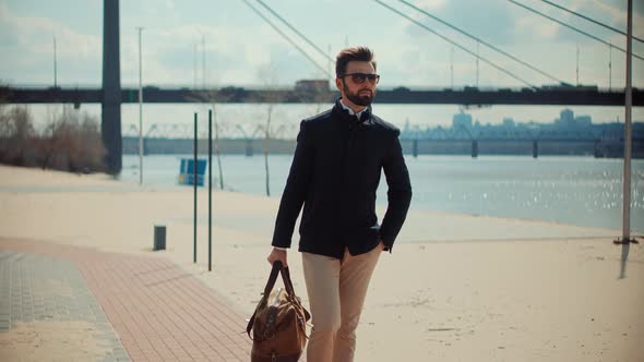 Elegant Businessman With Modern Bag Walking On City Beach. Well Dressed Stylish Man Relaxing.