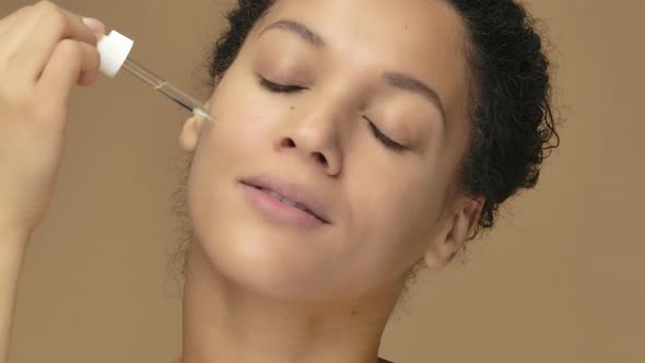 Beauty Portrait Young African American Woman Applying Skincare Serum on Face Rubbing Gently with