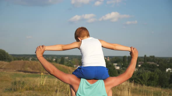 Cheerful Father Holding His Smiling Son on Shoulders and Spinning Around at Meadow on Sunny Summer