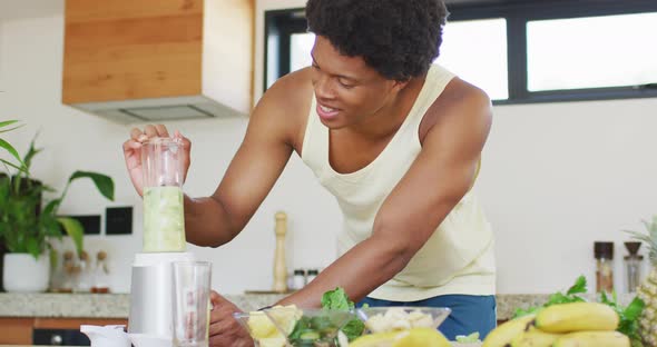 Fit african american man cooking, preparing healthy green smoothie