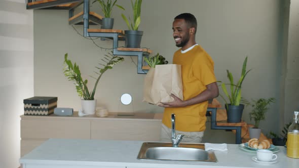 Slow Motion of Smiling African American Man Carrying Bag of Groceries Walking in Kitchen at Home