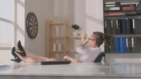 Woman office worker playing darts while sitting at workplace