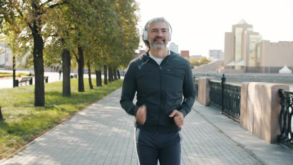 Dolly Shot of Mature Sportsman Jogging and Smiling Enjoying Healthy Activity Outdoors