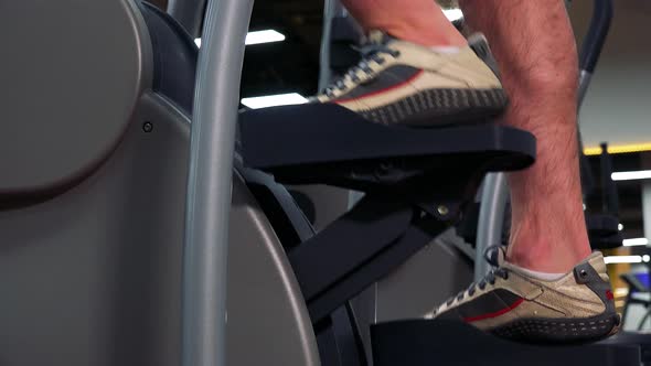 A Fit Man Trains on a Machine in a Gym - Closeup on the Feet From the Side