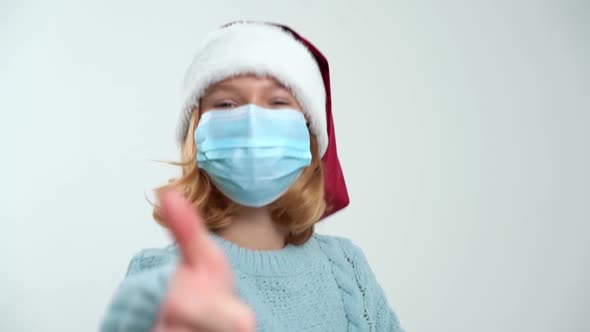 Happy Young Girl in Santa Claus Cap and Medical Mask Showing Like