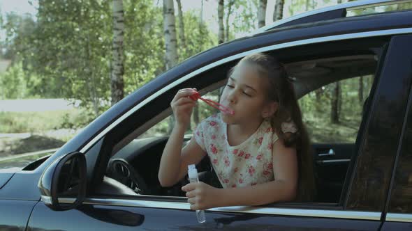 Little Cute Girl Blowing Soap Bubbles in the Car