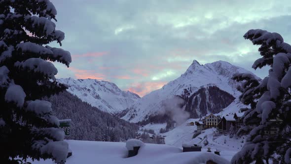 Evening in a Swiss Alps, the village of Samnaun. The smoking chimney on the snow-covered rooftop wit