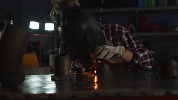 Female mechanic wearing welding helmet welding while sitting at car service station