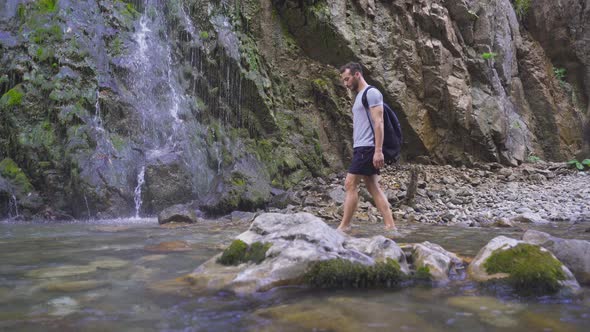 Man walking barefoot looks at the waterfall.