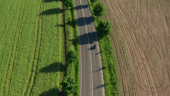 Motorcyclist Rides Between Plowed and Planted Fields