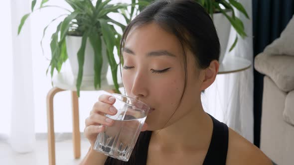 Close-up of pretty asian girl drinking water from glass after home workout exercise at home