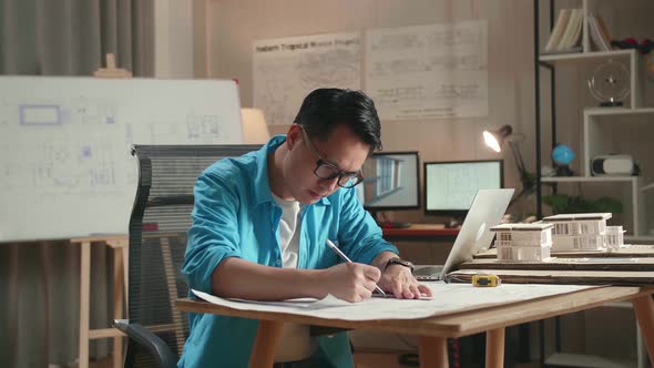 Asian Man Engineer With A Laptop Drawing Blueprint At The Office