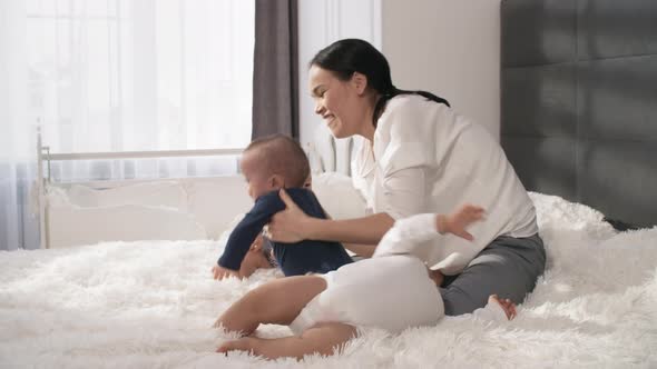 Happy Asian Mother Relaxing on Bed with Triplets