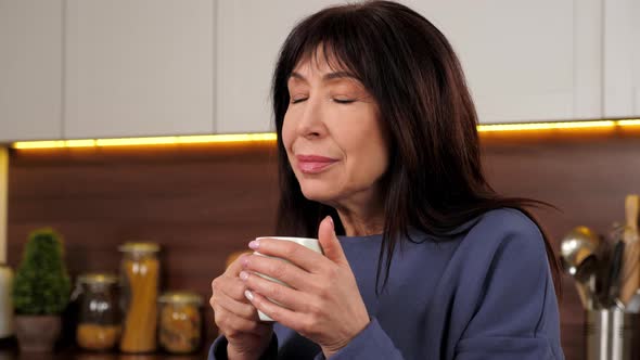 Aged Woman Drinking Delicious Warm Tea Coffee From Cup in Home Kitchen