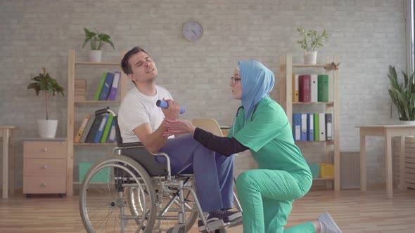 Nurse Muslim Woman in a Hijab Helps in the Rehabilitation of Disabled Person in a Wheelchair