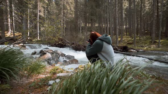 Happy Young Redhaired Woman Photographs a Mountain Forest and a River in the Dolomites Mountains