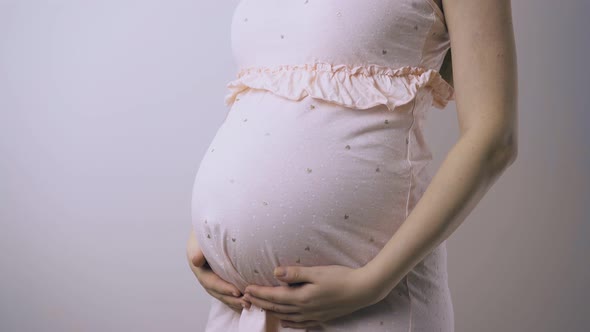 Pregnant Lady in Dress Touches Baby Bump at Wall Closeup