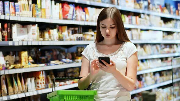 Beautiful Young Woman with Shopping Basket Use Phone in Supermarket, Texting
