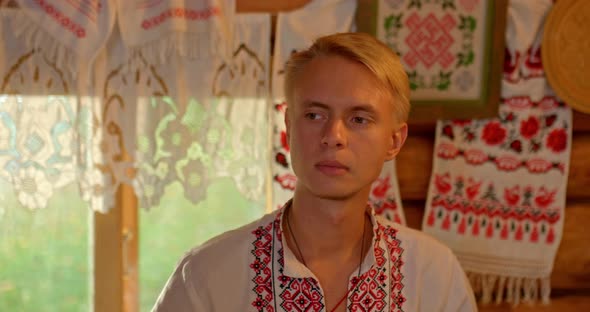 Portrait a Slavic Man in a National Costume in a Shirt with Embroidery Sits By the Window in a Hut