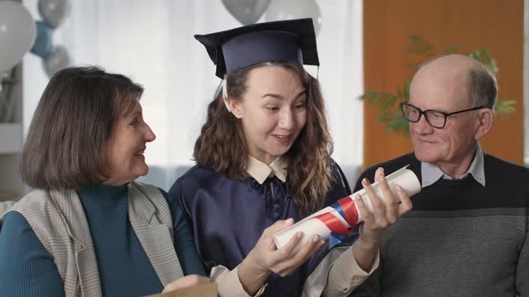 Cheerful Girl in Academic Hat and Gown Together with Joyful Parents Celebrates Graduation and