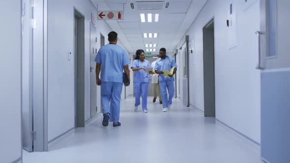 African american male and female doctor in discussion walking in busy hospital corridor